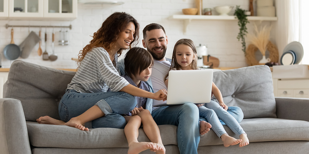 Happy family of four sat on a sofa, participating in user research on a laptop.