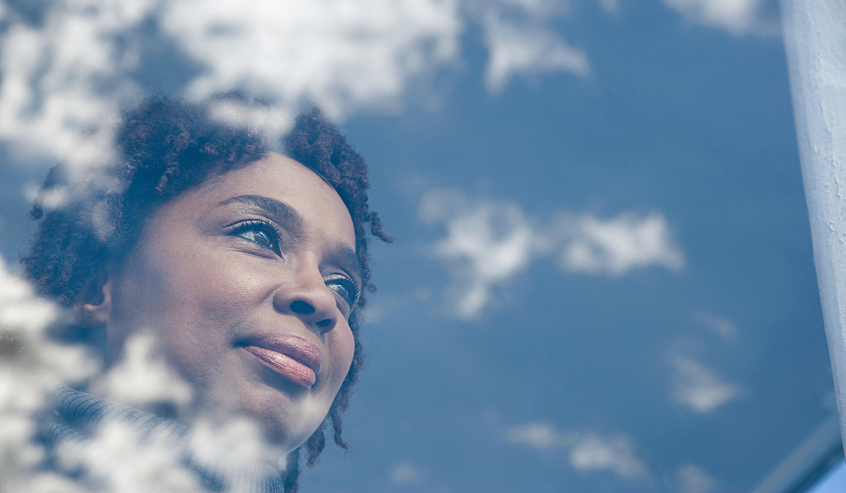 Person looking out of a window at a blue sky with clouds