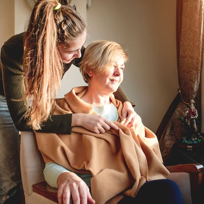 A social worker wrapping a blanket around an older woman in a chair