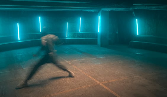 Still video image from Mustafas Story. A blurred picture of a person dancing in a room with neon lights