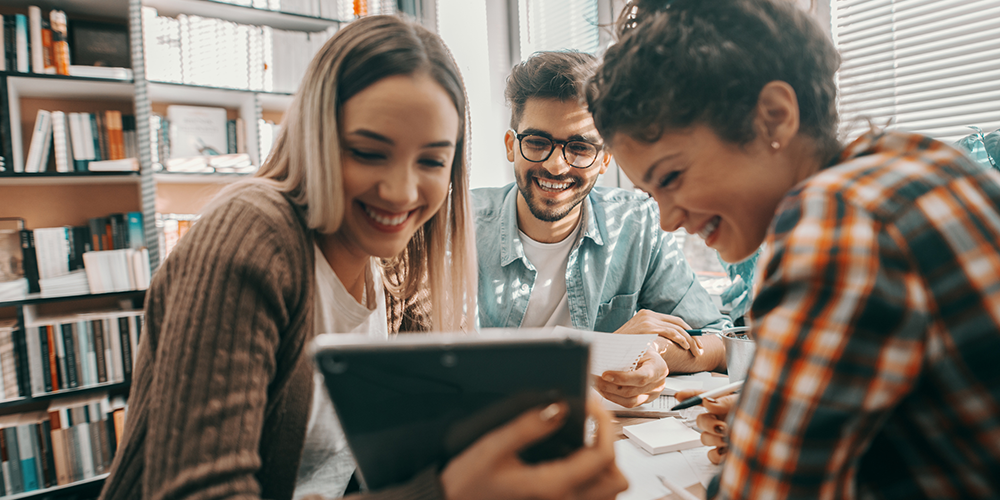 Three people laughing together around an iPad device