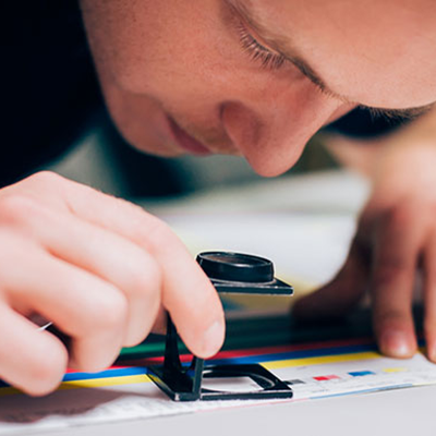 Man using a magnifying glass to inspect a print job.