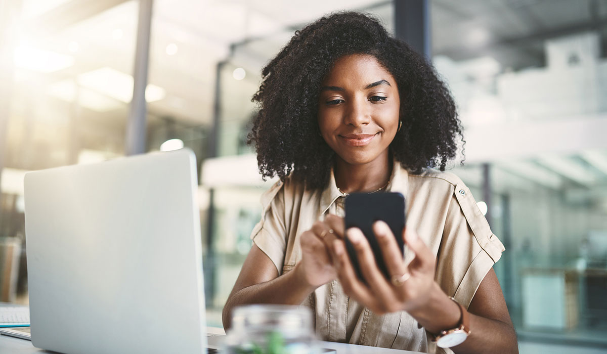 Woman sat a desk tapping on her mobile phone