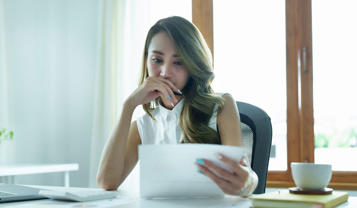 Portrait of a thoughtful Asian businesswoman looking at financial statements and making marketing plans using a computer on her desk Portrait of a thoughtful Asian businesswoman looking at financial statements and making marketing plans using a computer on her desk