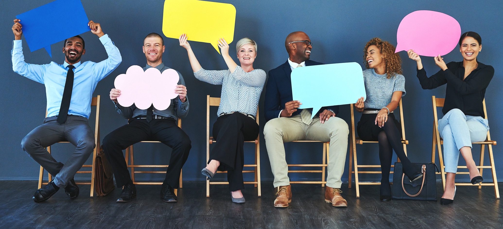 A group of people sat in a row holding up speech bubbles.